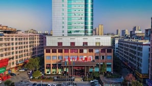 A modern hotel with a prominent glass facade, multiple floors, and a central entrance with flags. - Jin Li Hua Grand Hotel (Shaodong)