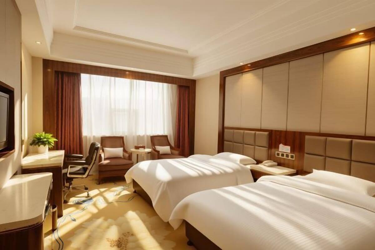 Une chambre d’hôtel avec deux lits, un bureau, une chaise, une télévision et une fenêtre avec des rideaux.