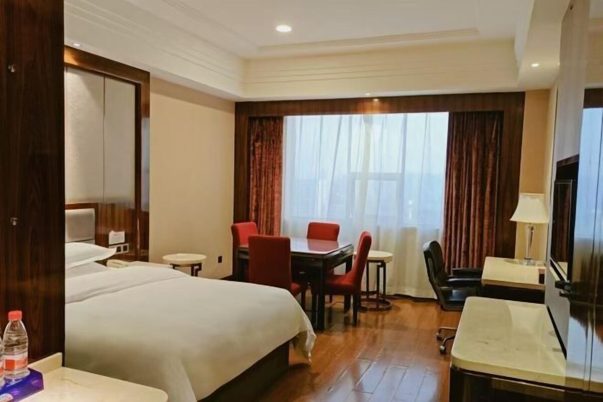 Habitación de hotel con cama, escritorio, silla, mesa y ventana con cortinas.