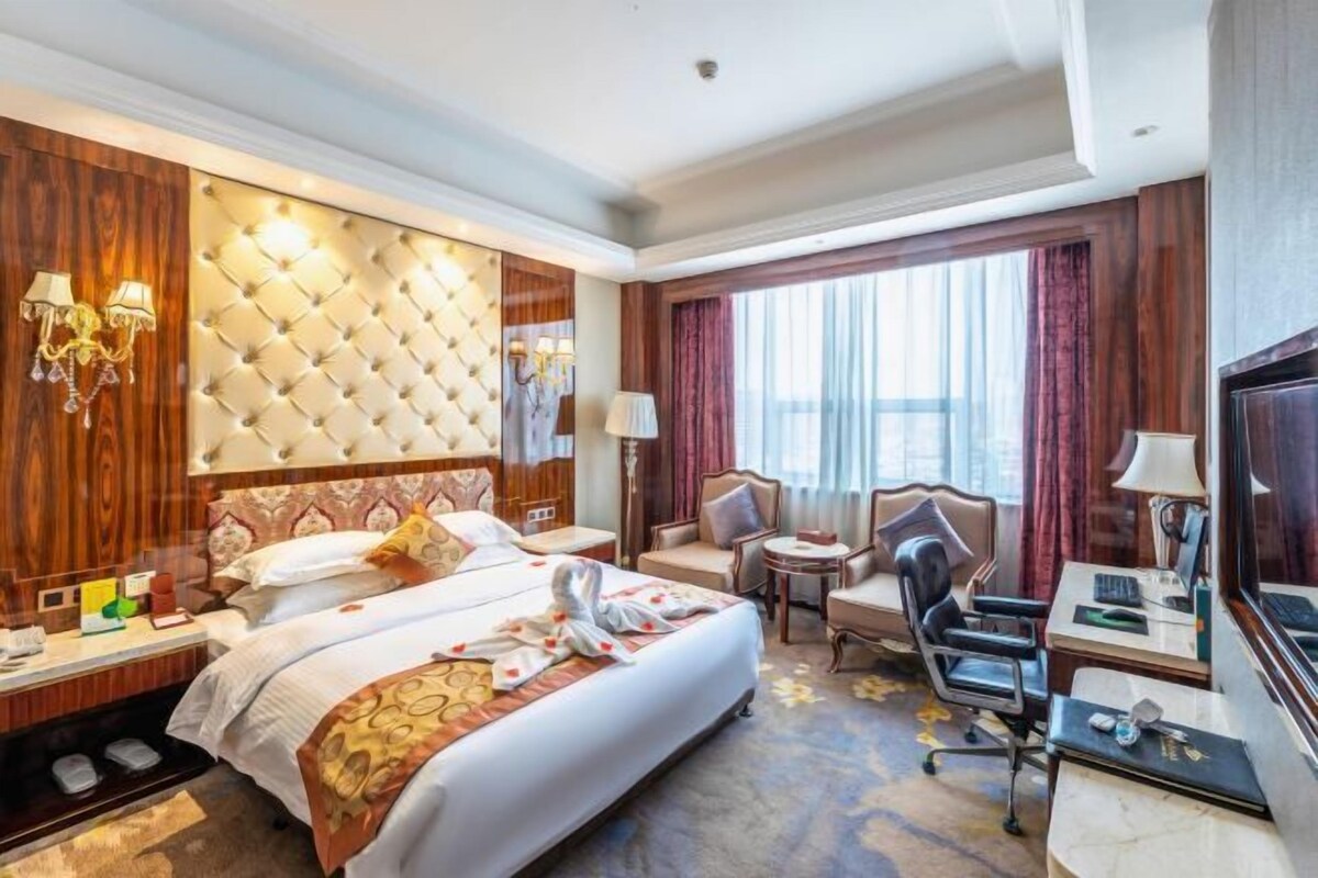 A hotel room with a large bed, a desk, a chair, a TV, and a window with curtains.