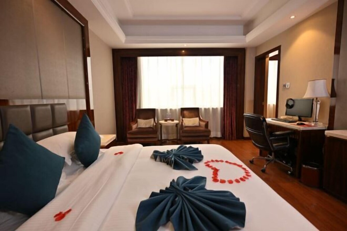 A hotel room with a large bed, a desk, a chair, and a small table.