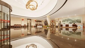 A modern hotel lobby with a reflective floor, a central chandelier, and a reception desk with artwork on the wall. - Jin Li Hua Grand Hotel (Shaodong)