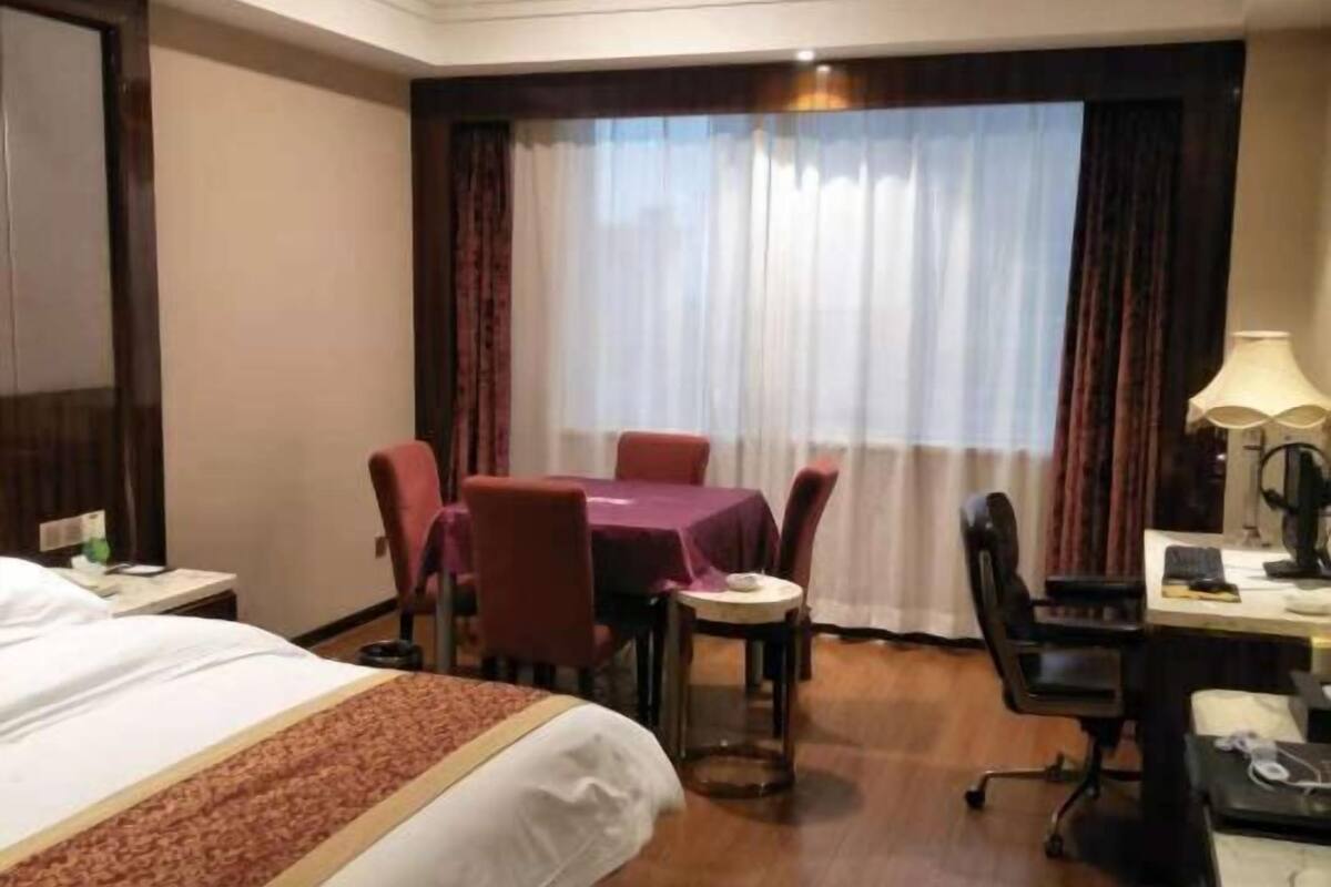 Une chambre d’hôtel avec un grand lit, un bureau avec un ordinateur, une chaise, une petite table et une fenêtre avec des rideaux.