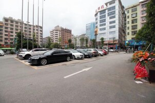 Un estacionamiento con varios autos, un edificio con un letrero y una calle con semáforos.
