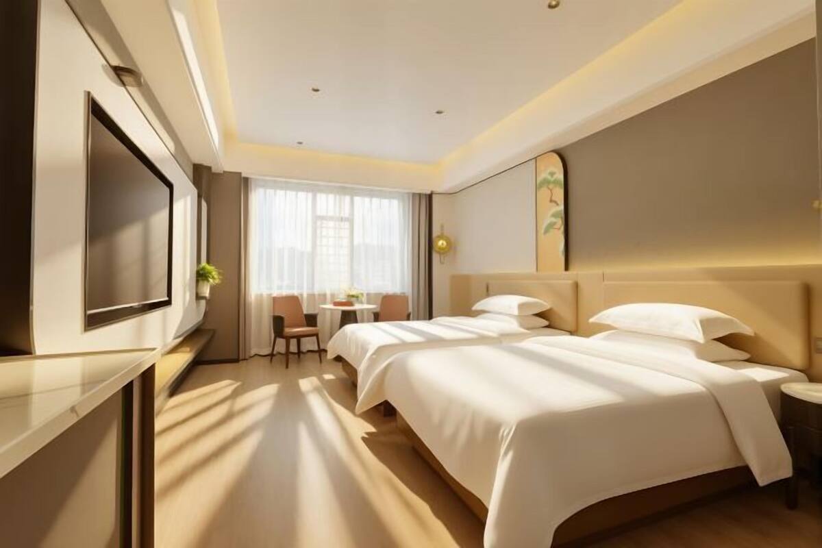 Une chambre d’hôtel avec un grand lit, un téléviseur fixé au mur, un bureau avec une chaise et une fenêtre avec des rideaux.