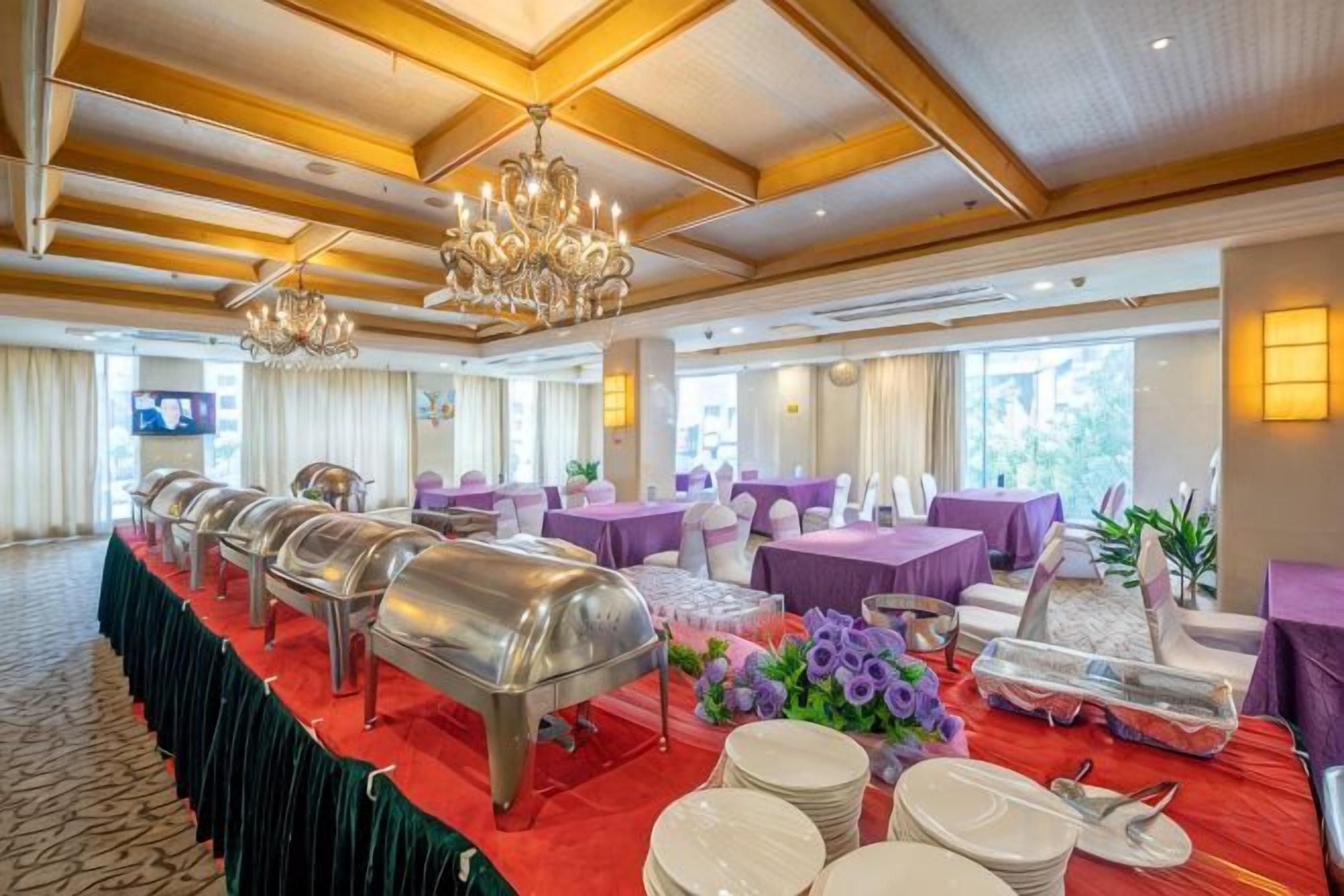 Een balzaal met een lange tafel, buffetten en paarse zitplaatsen.