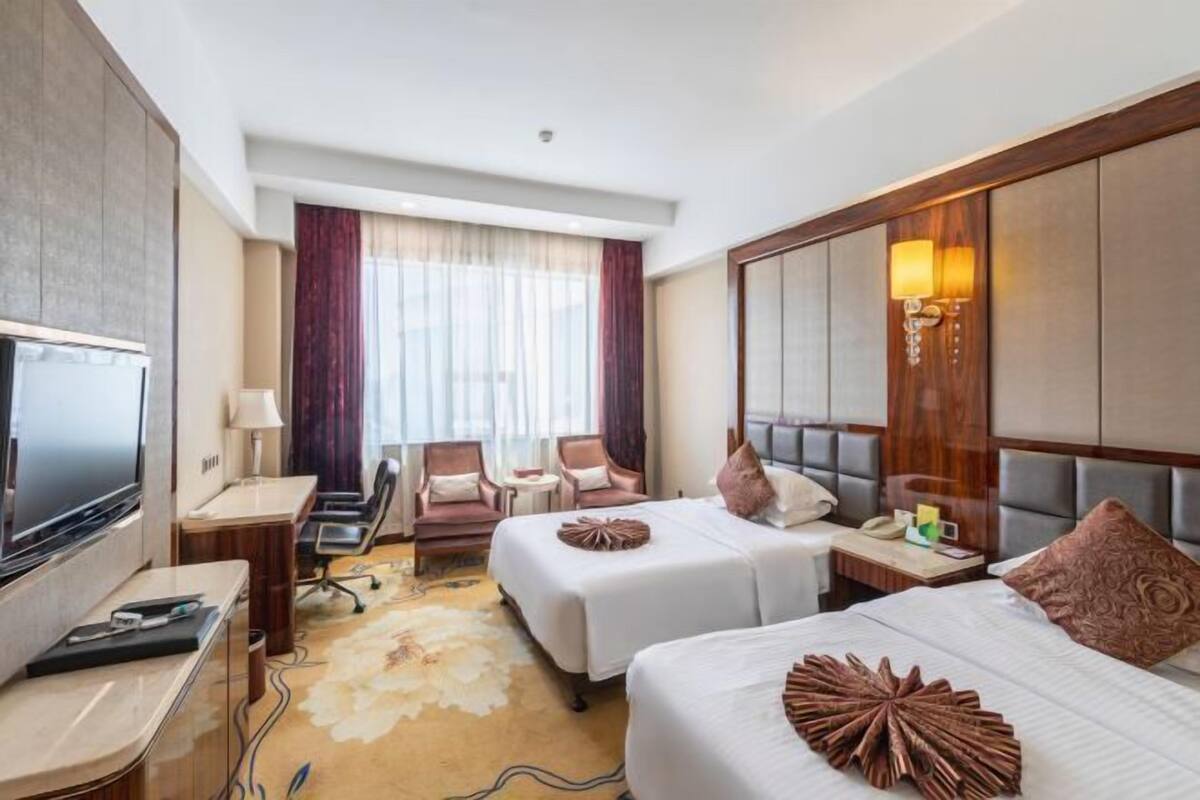 Une chambre d’hôtel avec deux lits, un bureau, une télévision et une grande fenêtre avec des rideaux.