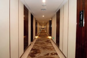 Un pasillo largo y estrecho con alfombra estampada, puertas de madera y un letrero que indica la habitación 1907.