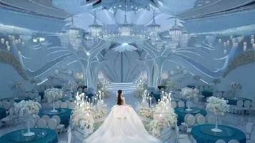 A wedding venue with a central aisle, round tables, and a chandelier.
