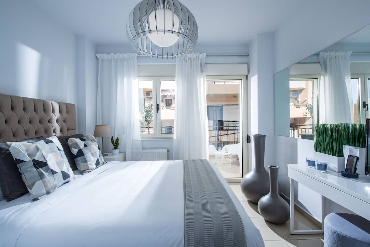 A modern bedroom with a large bed, a bedside table with a lamp, a dresser, and a large mirror.