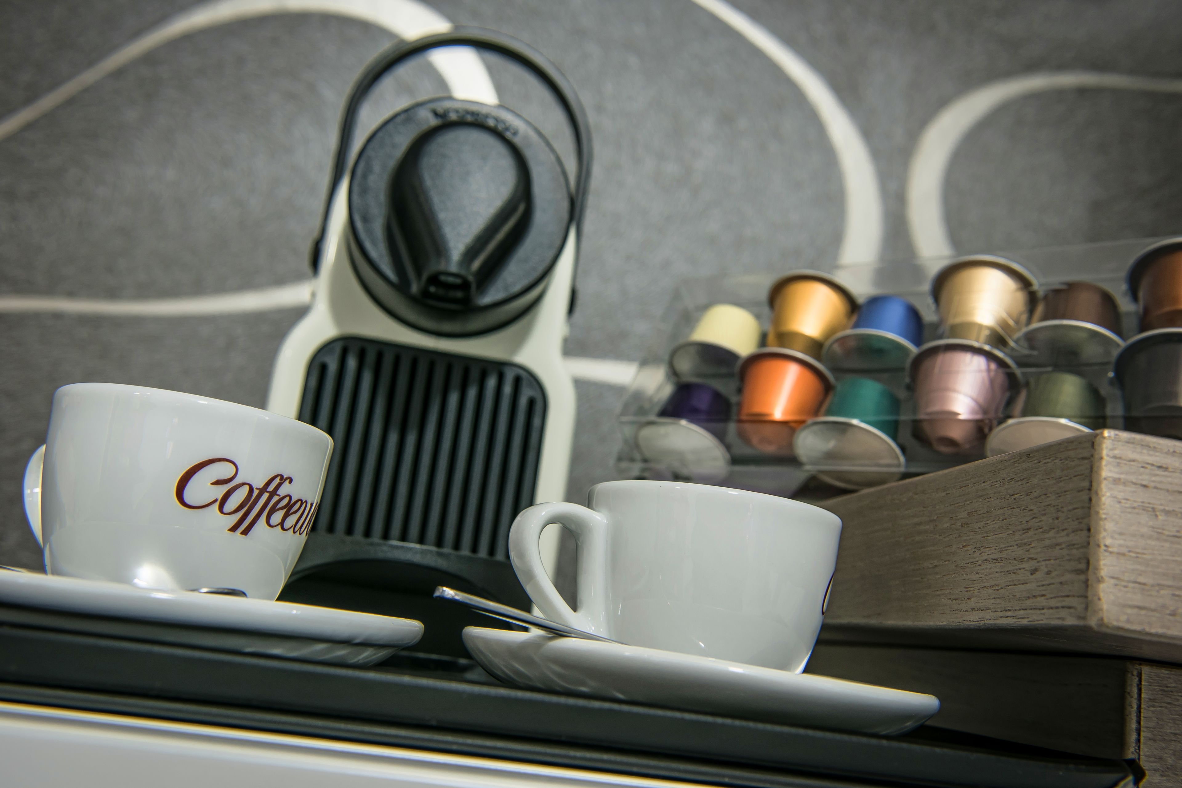 A coffee machine, two cups, and a container of coffee pods.