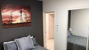 A bedroom with two beds, a painting of a sunset, and a door leading to another room. - Quelle Vue HUSKISSON - Means What a View in French - The only place to stay (Huskisson)