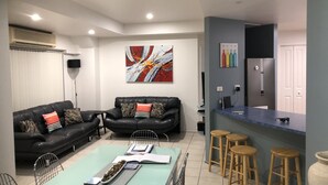 A modern living room with a black leather sofa, a dining table with chairs, and a kitchen area with stools. - Quelle Vue HUSKISSON - Means What a View in French - The only place to stay (Huskisson)