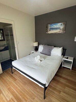 Ein Schlafzimmer mit Bett, Nachttischen, einer Lampe, einem Gemälde und einem Badezimmer mit Waschbecken und Dusche.