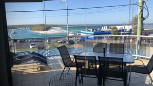 A dining area with a view of the sea and beach, featuring a table and chairs, and a sign for 'DUSKY BAKERY & CAFE'. - Quelle Vue HUSKISSON - Means What a View in French - The only place to stay (Huskisson)
