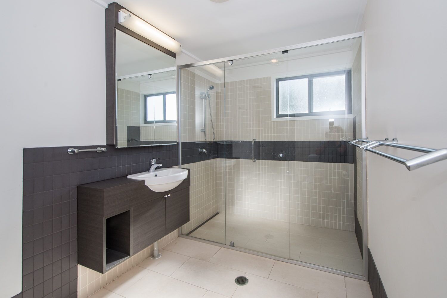 A modern bathroom with a glass-enclosed shower, a white sink, and a dark-toned vanity.
