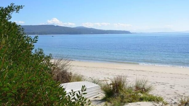 A beach with a wooden deck and greenery in the foreground. - Yolla Beach House A Quiet Relaxing Getaway (Bruny Island)
