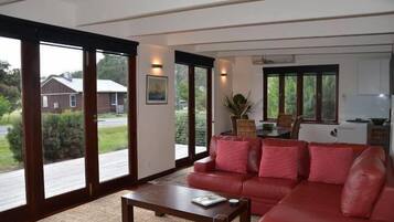 A living room with a red sofa, a coffee table, and a view of a house through large sliding glass doors.