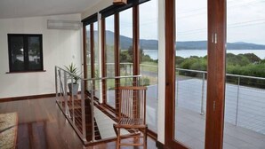 A spacious balcony with a wooden railing, a potted plant, and a view of a lake and mountains. - Yolla Beach House A Quiet Relaxing Getaway (Bruny Island)