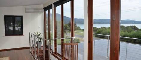A spacious balcony with a wooden railing, a potted plant, and a view of a lake and mountains.