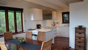 A modern kitchen with white cabinets, a central island, and a dining area with wicker chairs. - Yolla Beach House A Quiet Relaxing Getaway (Bruny Island)