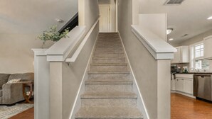 Un escalier avec des marches recouvertes de moquette, des murs blancs et un coin cuisine équipé d’un lave-vaisselle et de placards.