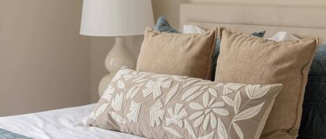 A bed with a white and blue quilt, two beige pillows, and a white lamp beside it.