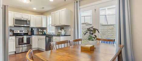 A modern kitchen with white cabinets, stainless steel appliances, and a dining area with a wooden table and chairs.