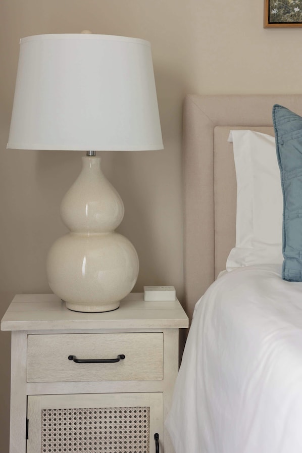 A bed with white bedding and a blue pillow, a white bedside table with a lamp, and a drawer with a handle.
