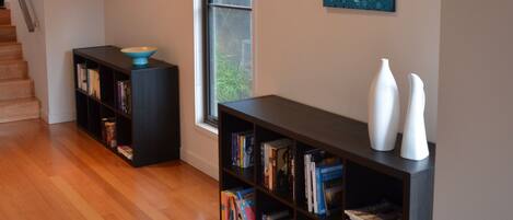 A modern interior with wooden flooring, a staircase, and two bookshelves with books and decorative items.