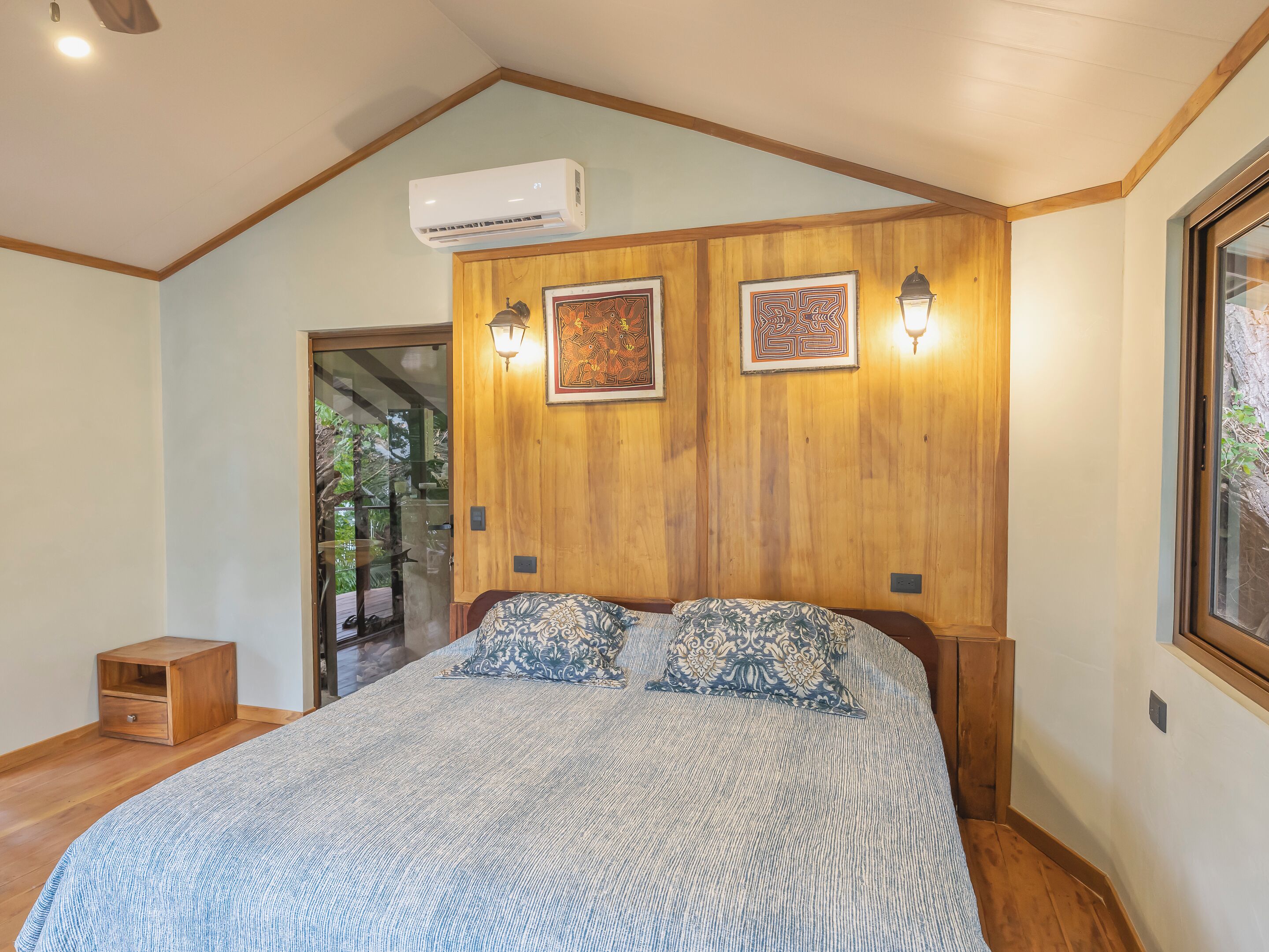 A bedroom with a large bed, wooden panel walls, two wall-mounted lights, and a ceiling fan.