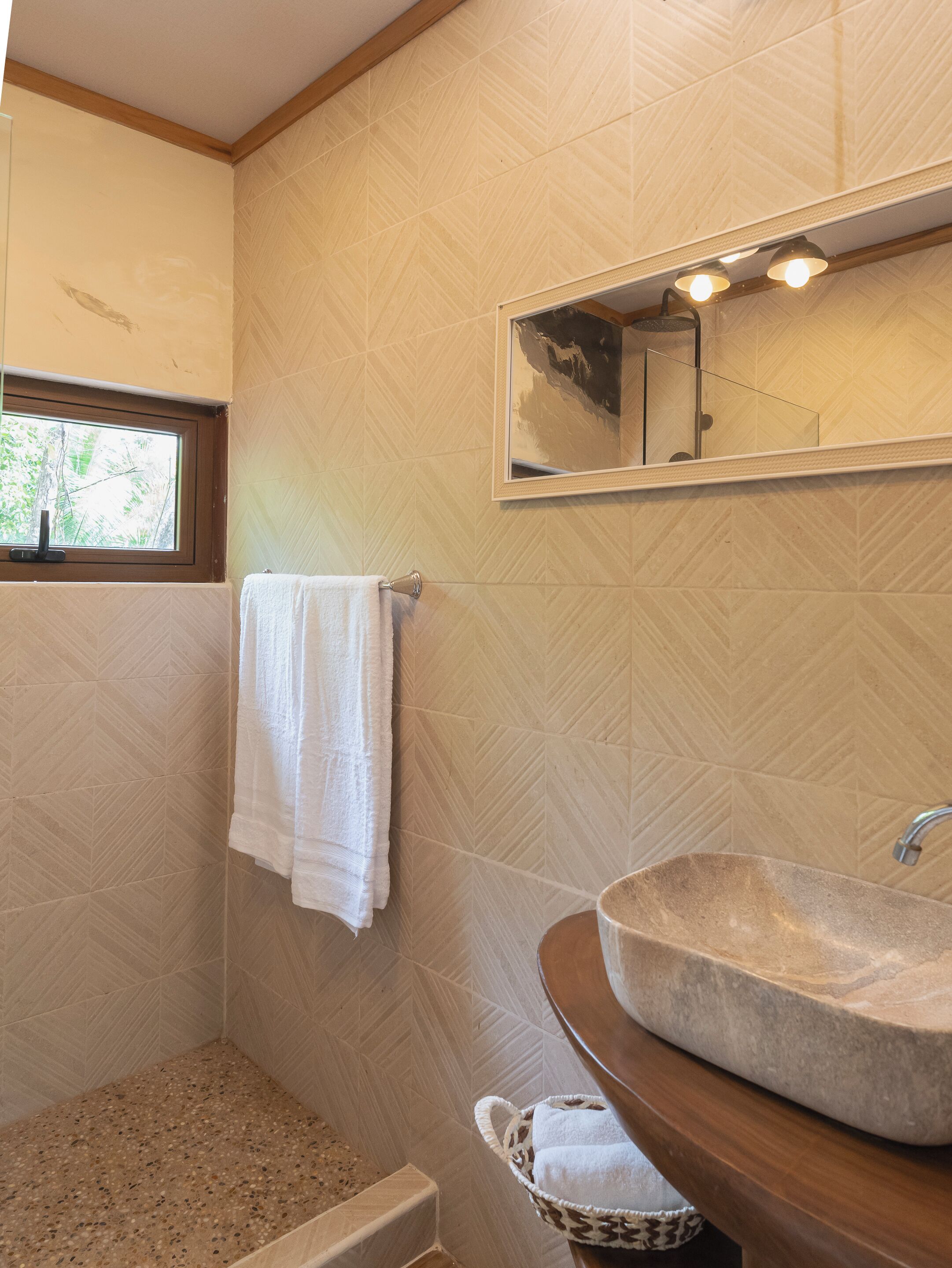 Un baño con pared de diseño en patrón de espiga, un espejo grande, un lavabo de piedra y una ventana.