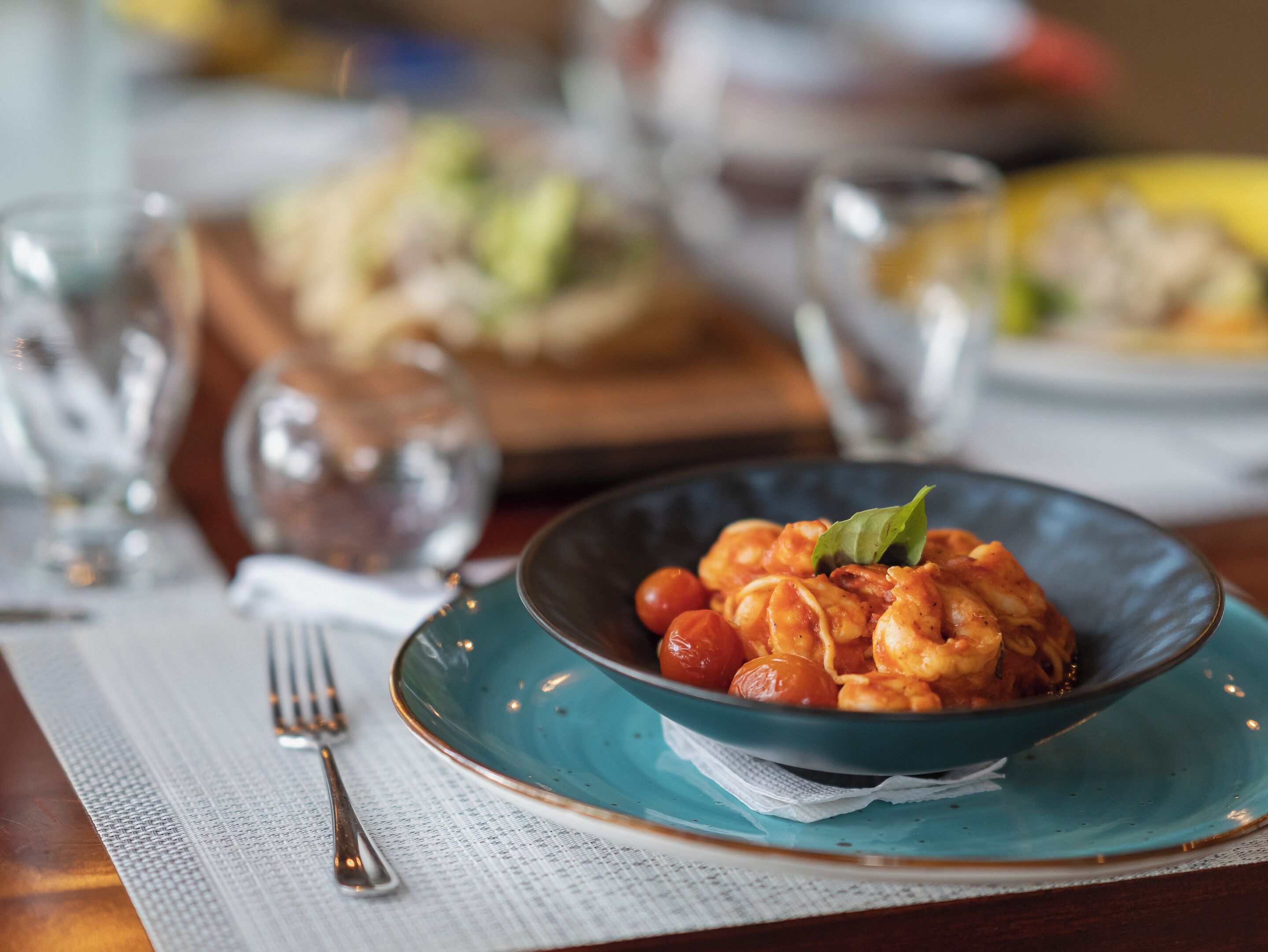 Ett matbord med en tallrik pasta, en gaffel och ett glas vatten.