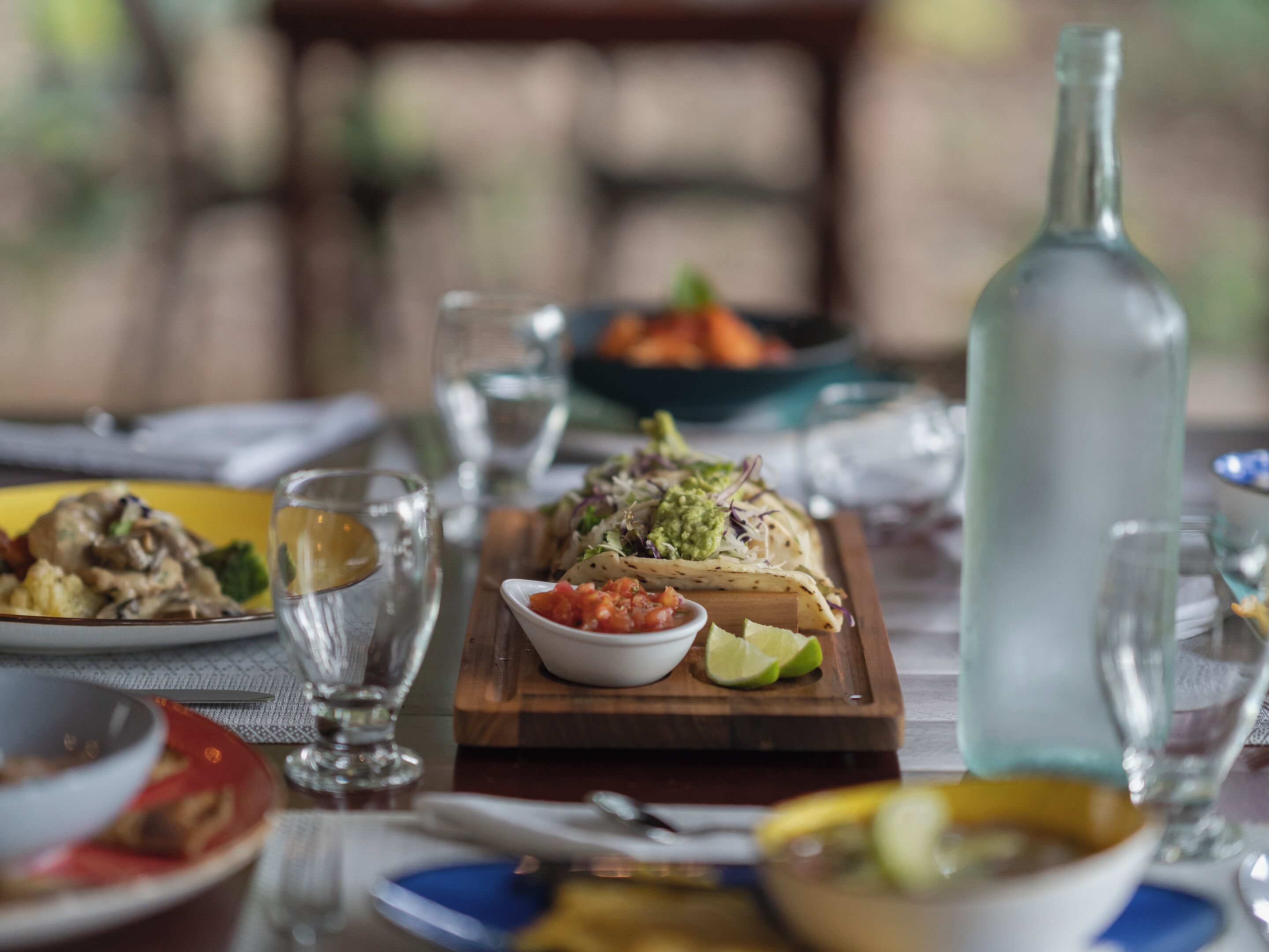 A dining table with various dishes, including tacos, a bowl of salsa, and a bottle of water.