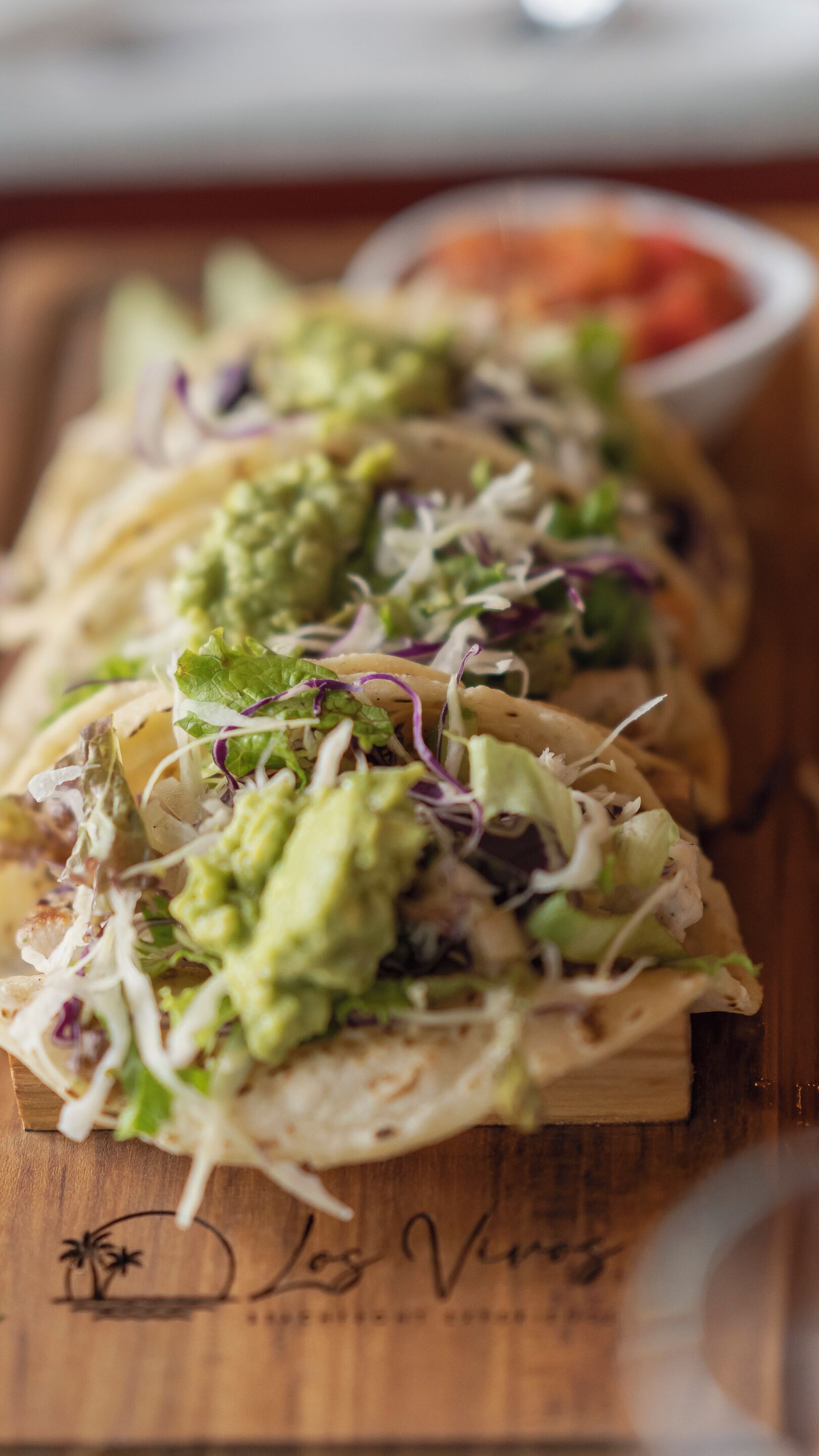 Tre tacos på en träbricka, med en handskriven skylt under.