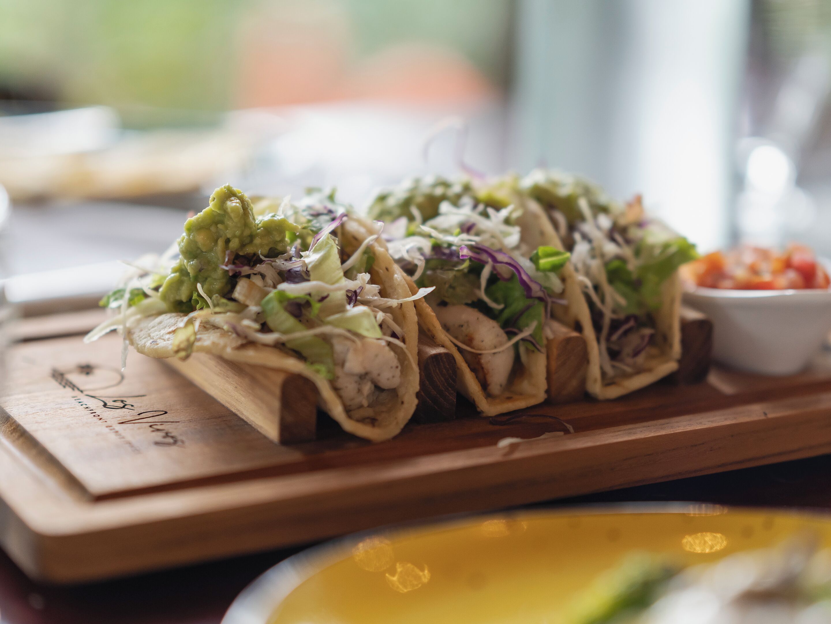 A wooden serving board with three tacos on it.