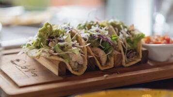 A wooden serving board with three tacos on it.