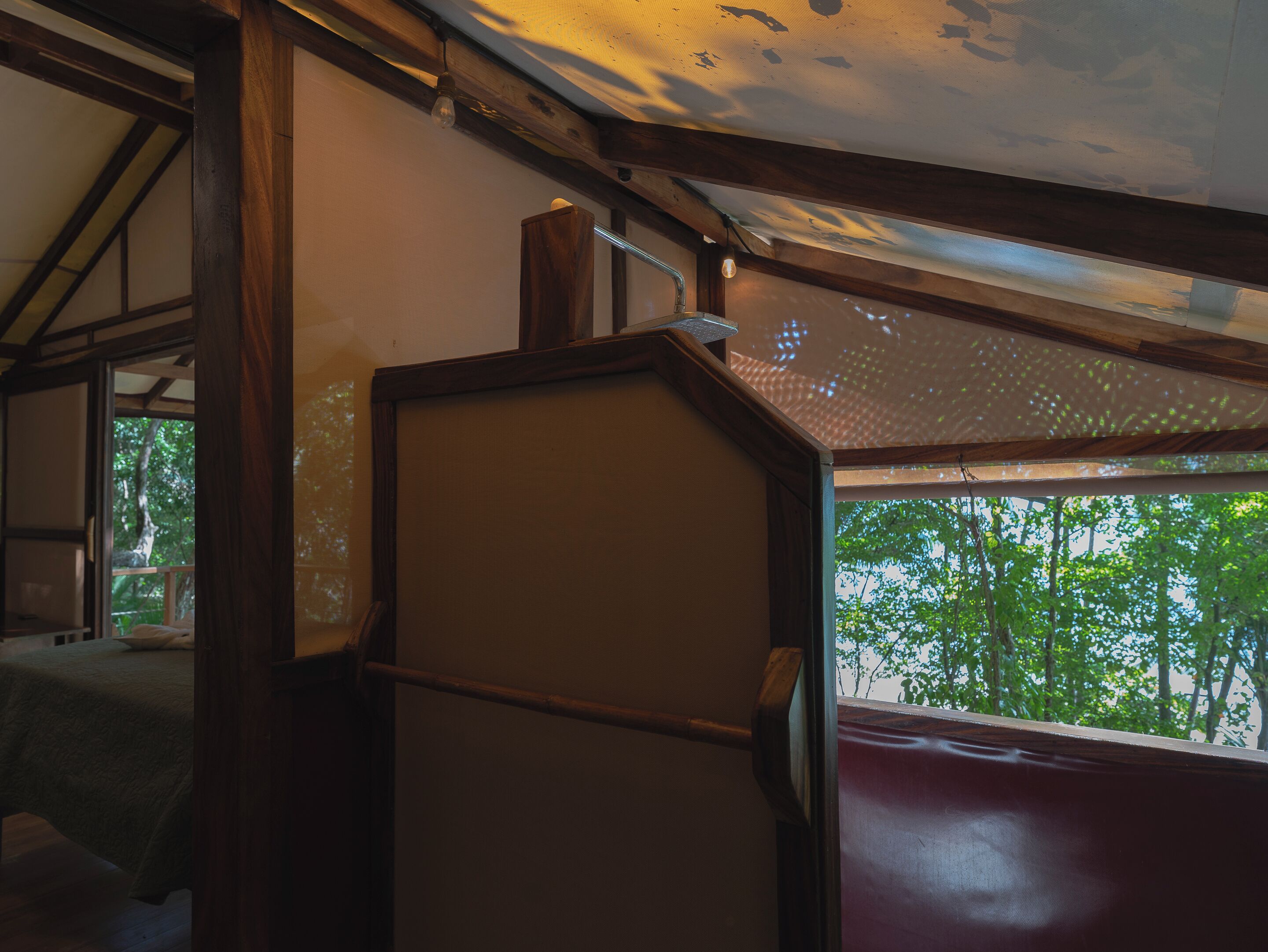 A room with a wooden ceiling, a bed with a green blanket, and a view of trees through a window.
