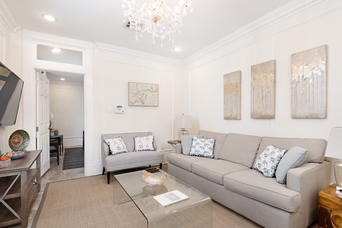 A modern living room with a grey sofa, a glass coffee table, and a chandelier.