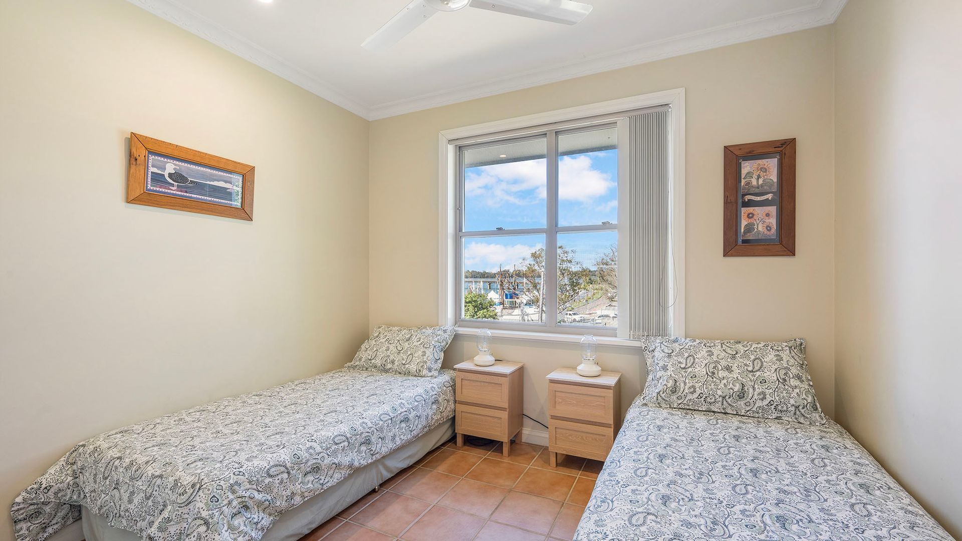 A bedroom with two single beds, a window with a view of boats, and two bedside tables.