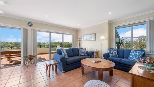 Un vaste espace de vie comprenant un ensemble de canapés, une table basse et une vue sur un balcon avec une table de patio.