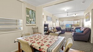 A dining area with a table set for four, a living room with a sofa and a television, and a view of the sea through the window.