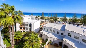 A coastal hotel with multiple white buildings, a parking area, and a view of the ocean.