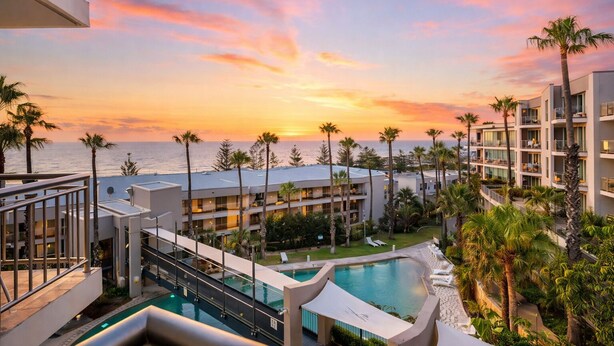 A resort with a pool, palm trees, and a view of the ocean at sunset.