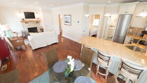 A modern kitchen with a central island, a dining area with round tables, and a living room with a fireplace.