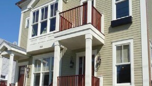 A two-story house with a front porch, a small balcony, and a stone foundation.