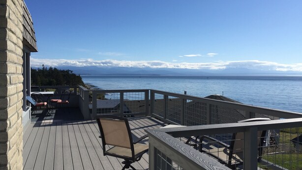 Une terrasse en bois, agréée de mobilier d’extérieur, qui offre une vue sur une étendue d’eau et sur des montagnes lointaines.