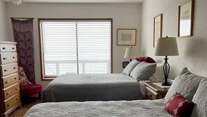 Une chambre avec deux lits, une commode, une table de chevet, une lampe et une fenêtre avec des stores.