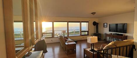 A spacious living room with large windows, a sofa, a TV, and a fireplace.