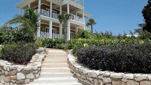 Un edificio de varios pisos con balcones, rodeado de muros de piedra y plantas tropicales.